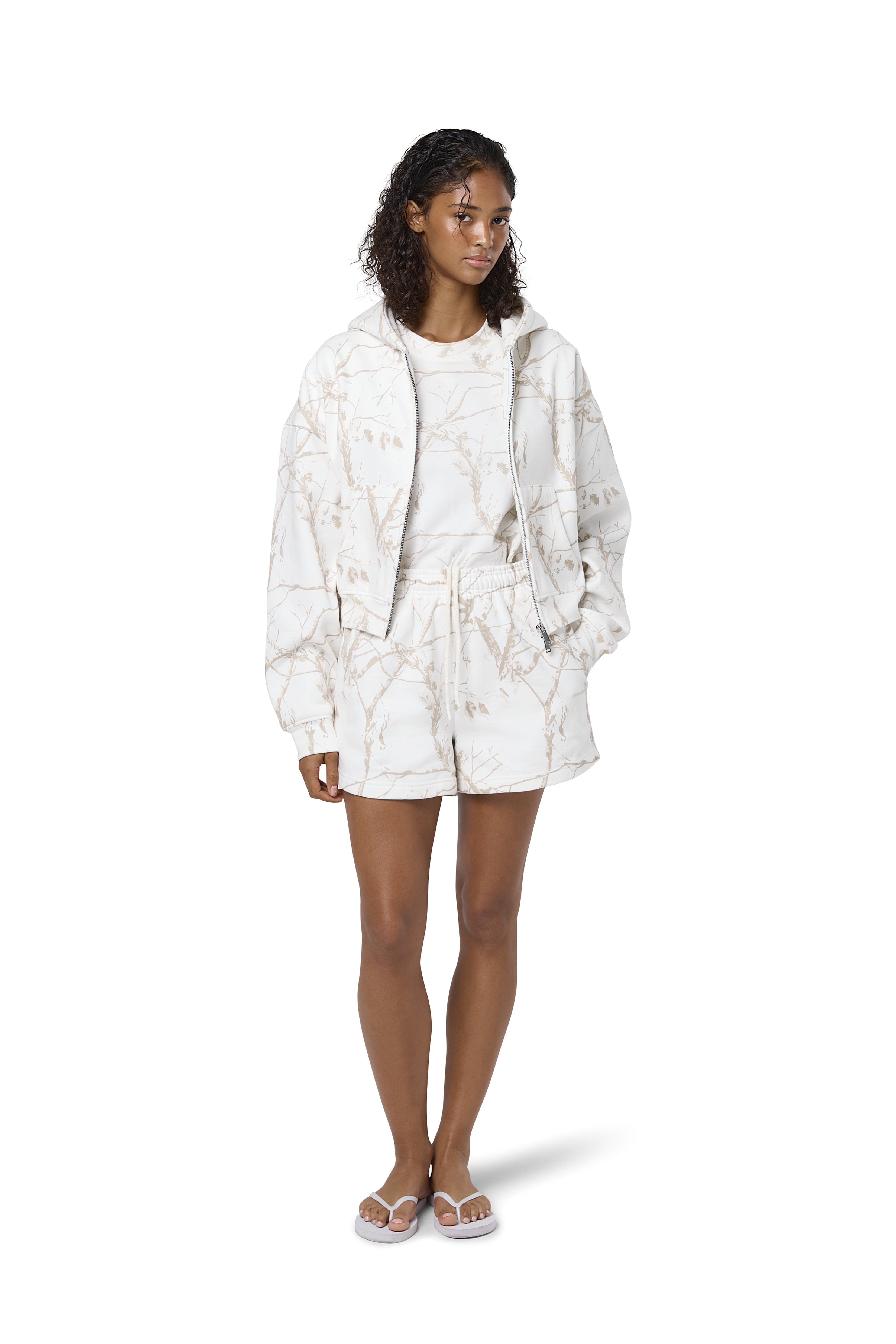 Women's high-waisted white lounge shorts with twig camouflage print, adjustable drawcord waist, and Sisters and Seekers logo to the hip